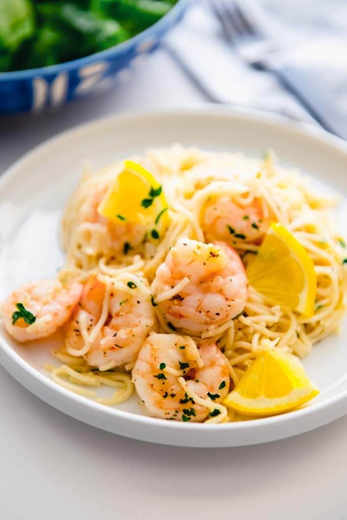lemon garlic shrimp pasta on a white plate with lemon slices