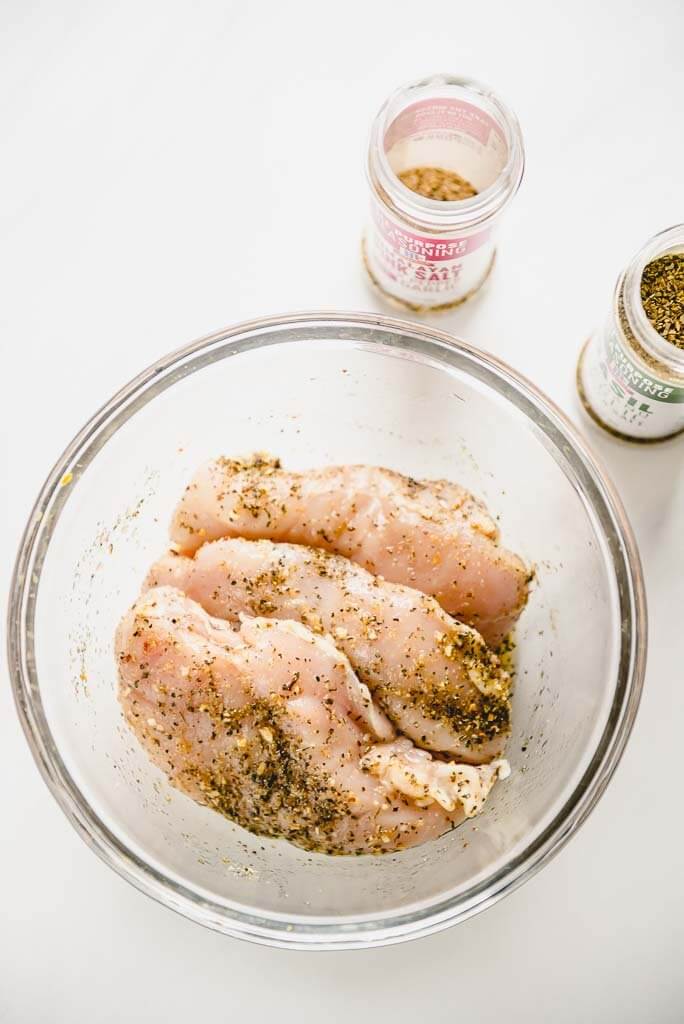 3 chicken breasts in glass bowl with seasoning blend bottles
