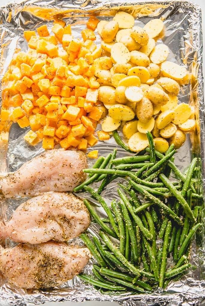chicken, green beans, potatoes and butternut squash on a sheet pan ready to cook