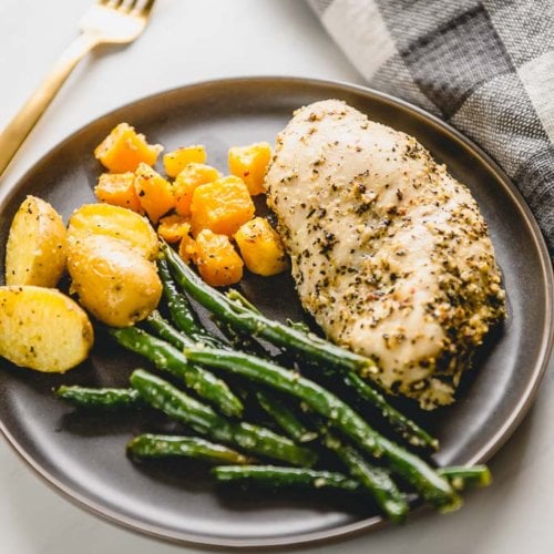 chicken breast with green beans potatoes and butternut squash on a gray plate with a gold fork