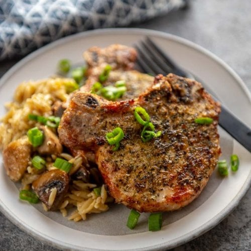 herb crusted pork chops on white plate topped with chopped green onions
