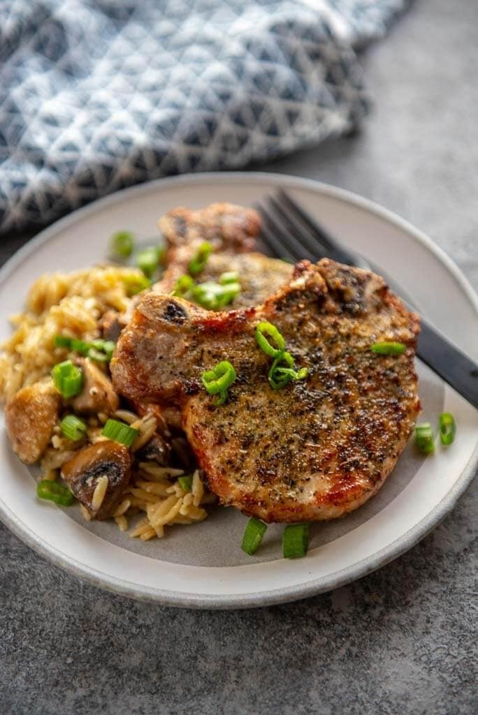 herb crusted pork chops on white plate topped with chopped green onions