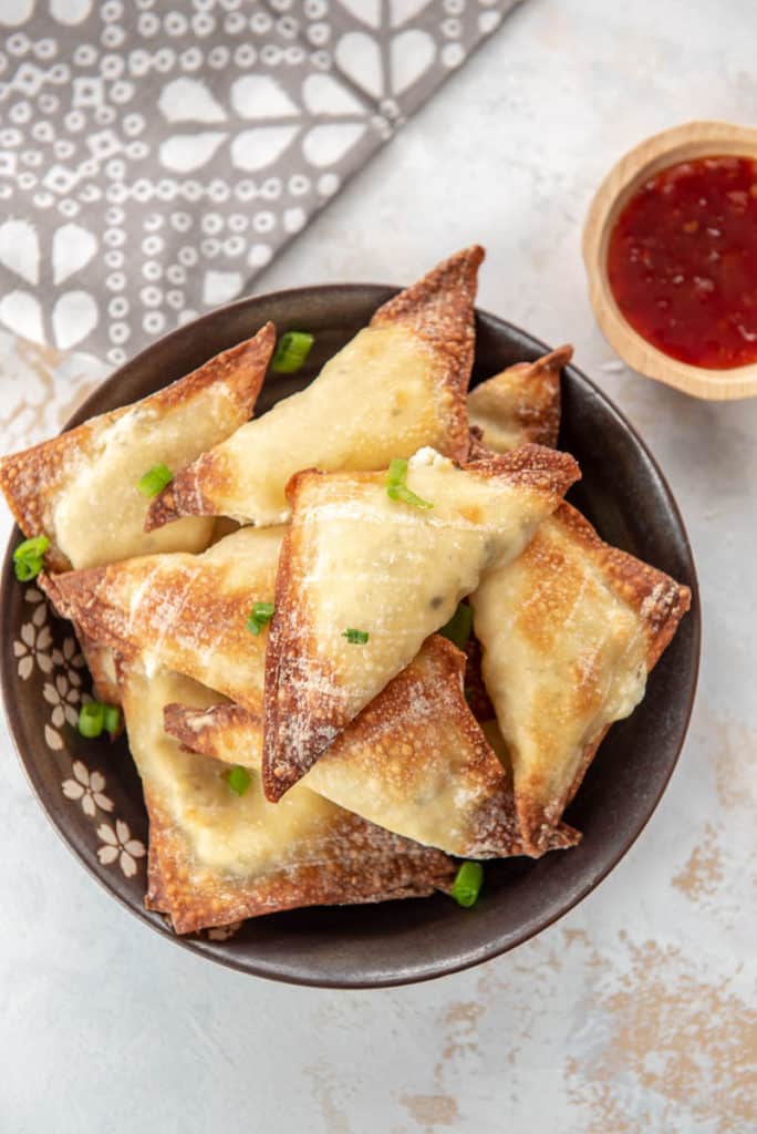 crab Rangoon on a plate next to sweet and sour sauce