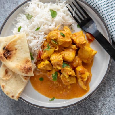 butter chicken with rice and naan on white plate