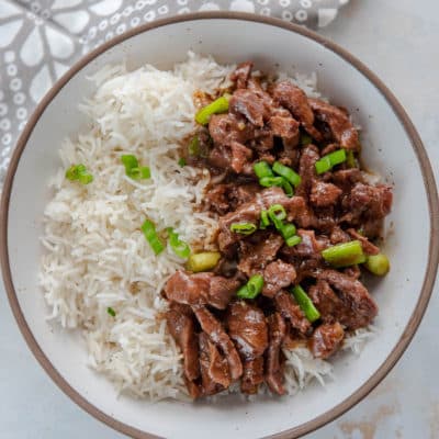 Mongolian beef with rice and green onions in white bowl