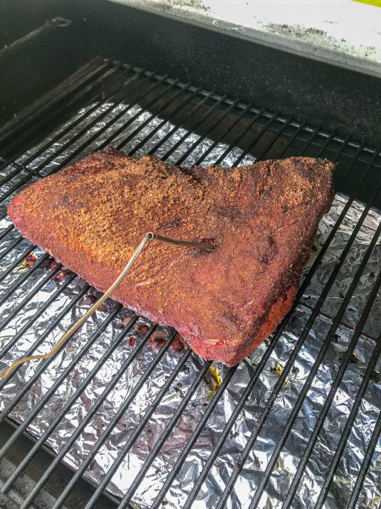 brisket on grate of pellet smoker with thermometer