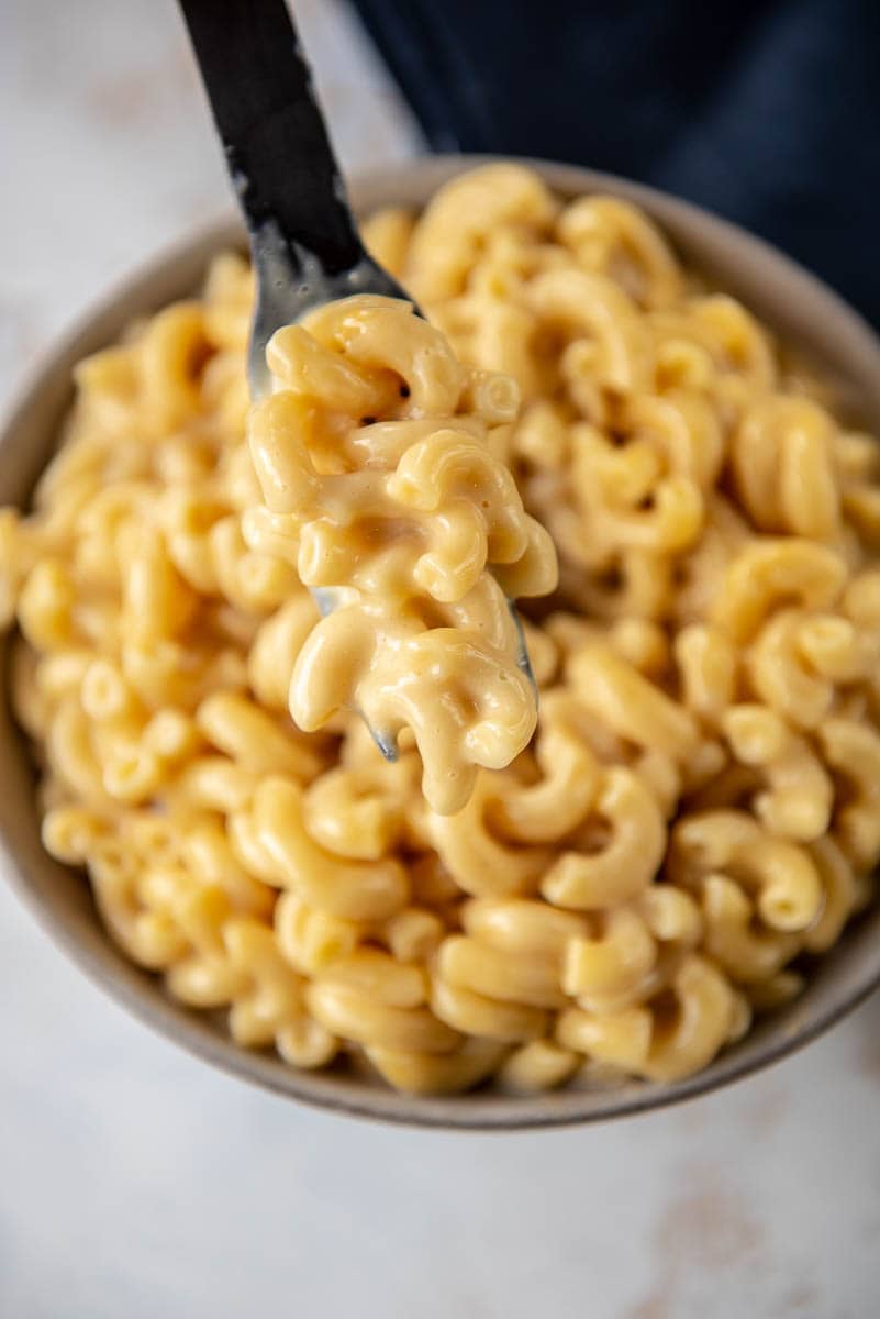 Mac and cheese on black fork over gray bowl