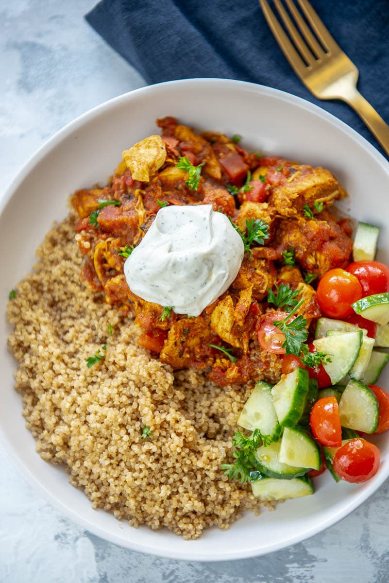 bowl filled with quinoa, moroccan chicken, tomatoes, cucumbers and yogurt sauce