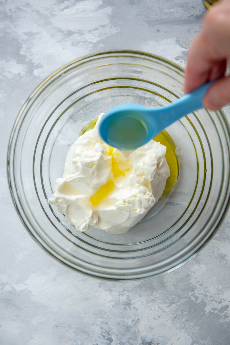 adding olive oil to yogurt in glass bowl
