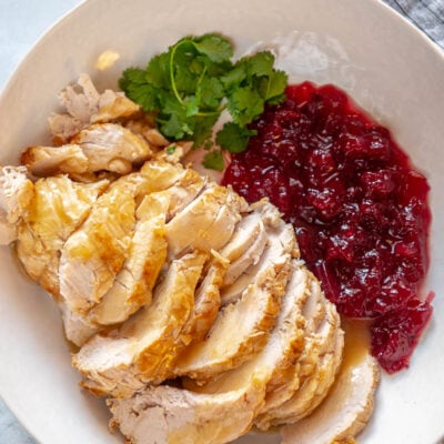serving bowl filled with sliced turkey breast topped with gravy and side of cranberry sauce