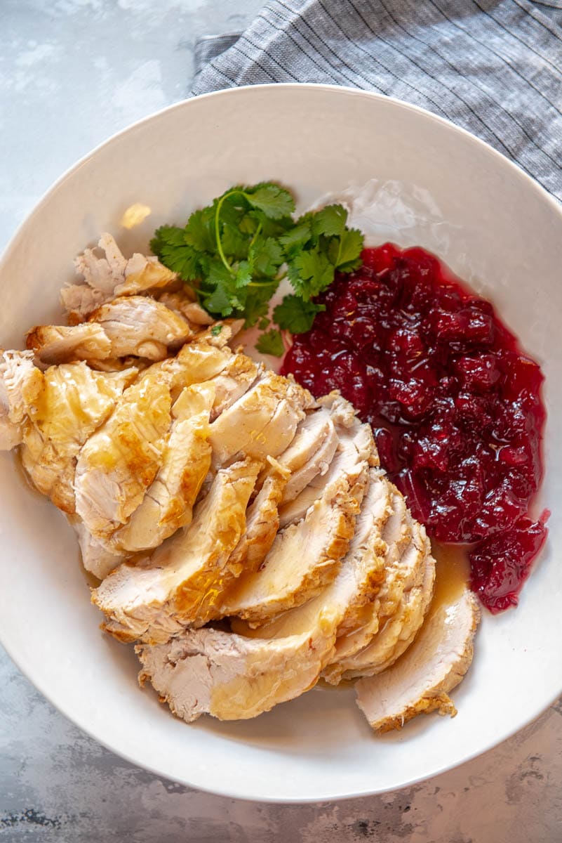serving bowl filled with sliced turkey breast topped with gravy and side of cranberry sauce