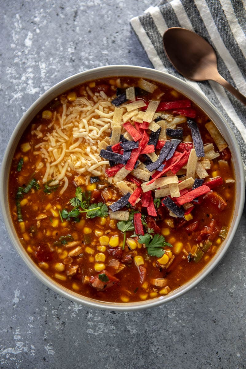 turkey tortilla soup in gray bowl topped with cheese and tri-color tortilla strips