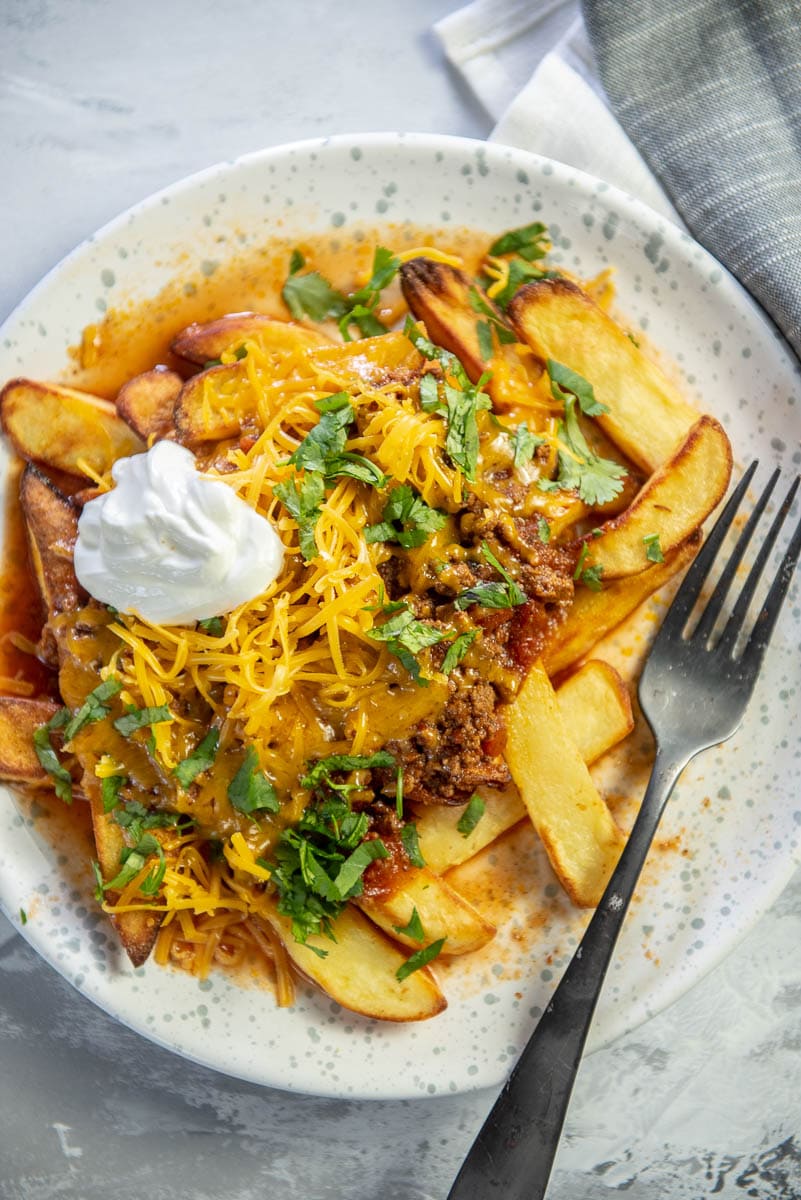 fries topped with chili on white and blue dotted plate