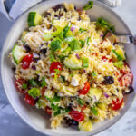 orzo salad with tomatoes cucumbers and feta in gray and white serving bowl
