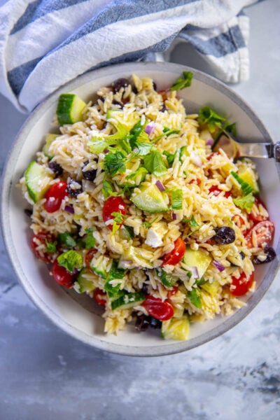 orzo salad with tomatoes cucumbers and feta in gray and white serving bowl