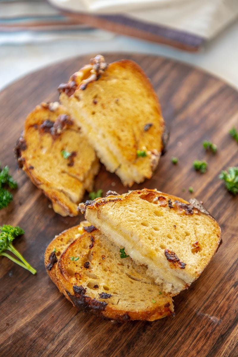 sourdough grilled cheese sandwich halves arranged on wood platter with parsley garnish