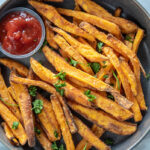 gray bowl with sweet potato fries and a container of ketchup