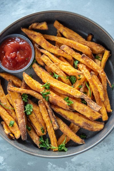 gray bowl with sweet potato fries and a container of ketchup