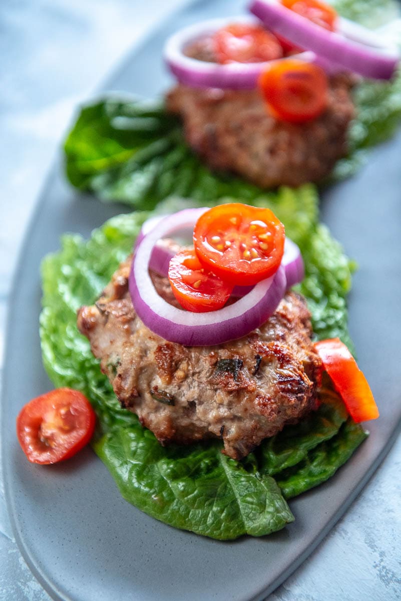 gray platter with lettuce wrapped turkey burger patties with tomato and onion