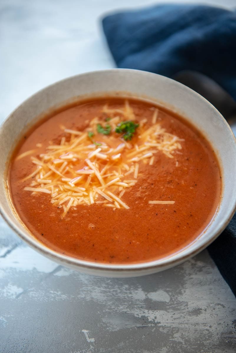 gray bowl of tomato soup with shredded parmesan on top