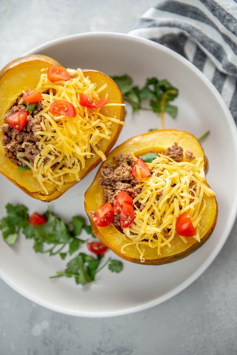 acorn squash halves with taco meat, cheese, and tomatoes on a white plate