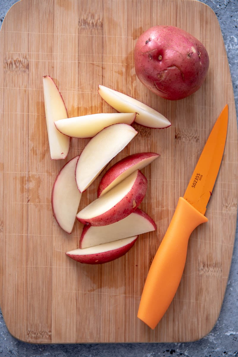 red skinned potato slices on a cutting board with an orange knife