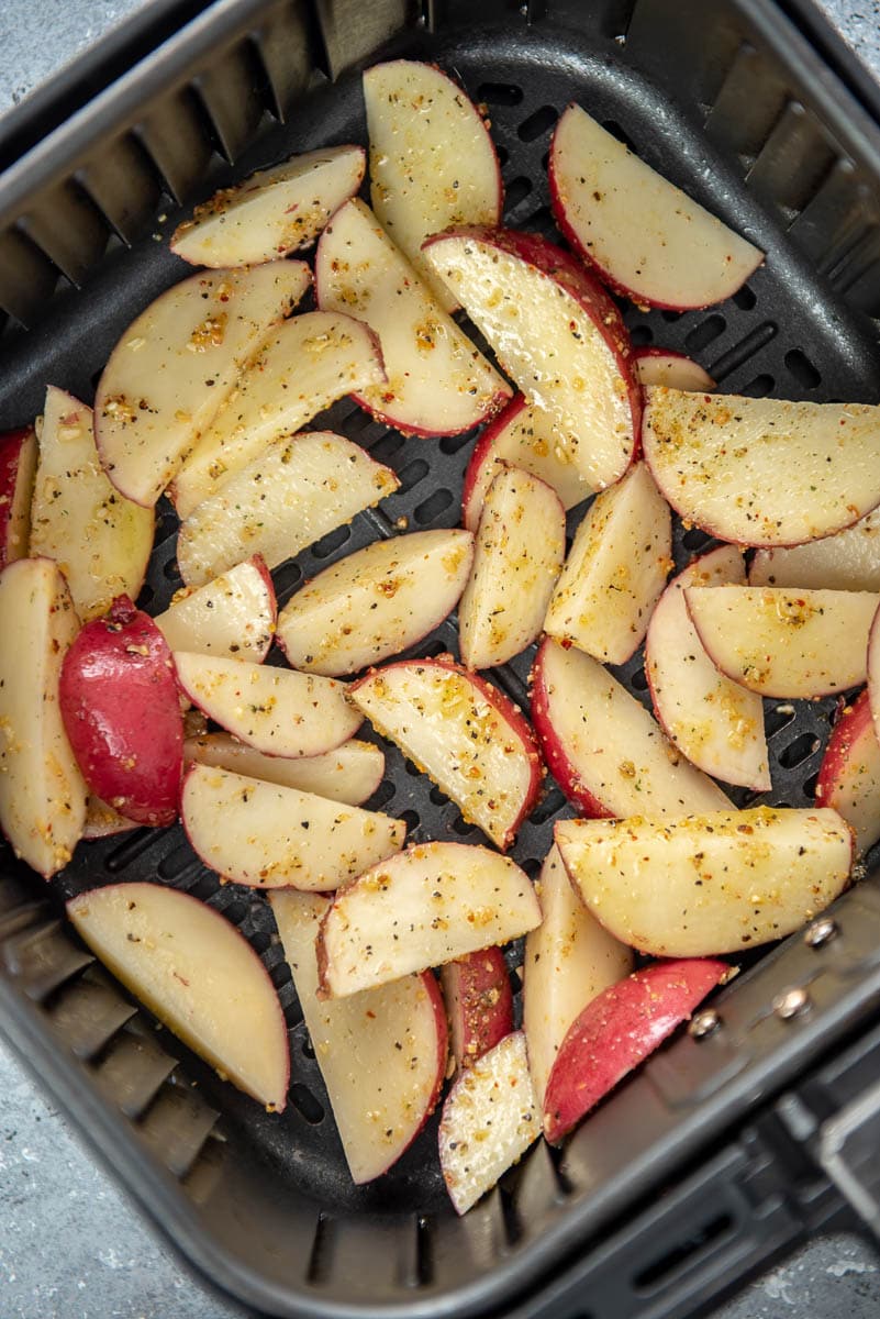 air fryer basket with seasoned potato wedges ready to cook