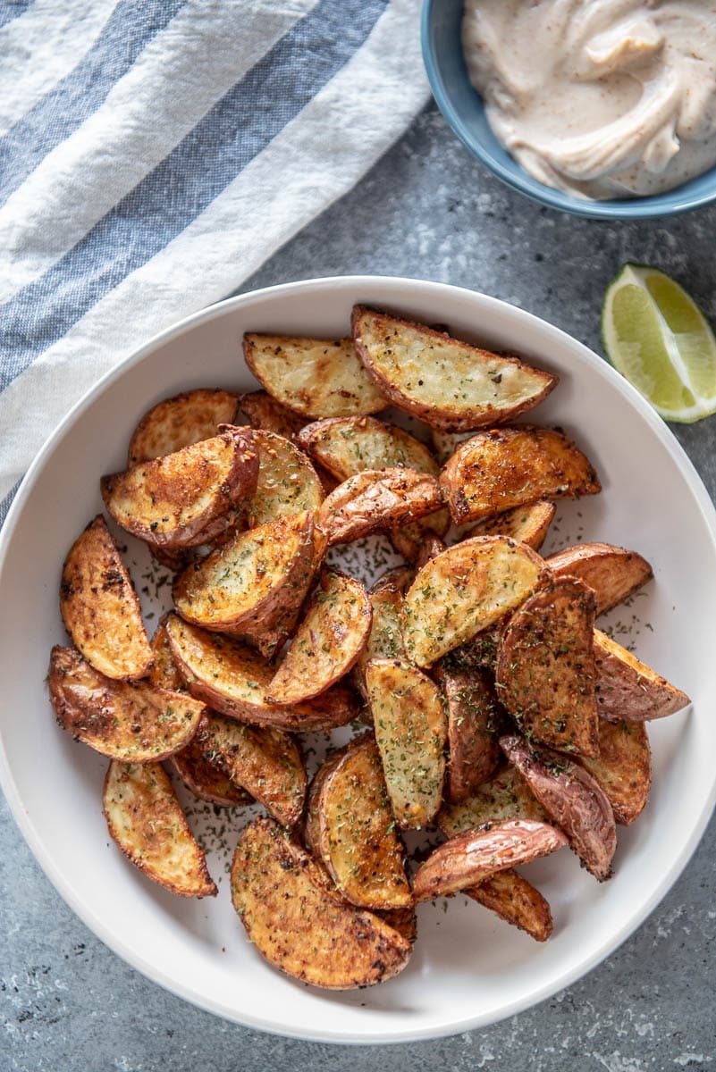 seasoned potato wedges in white bowl next to dipping sauce and a lime wedge