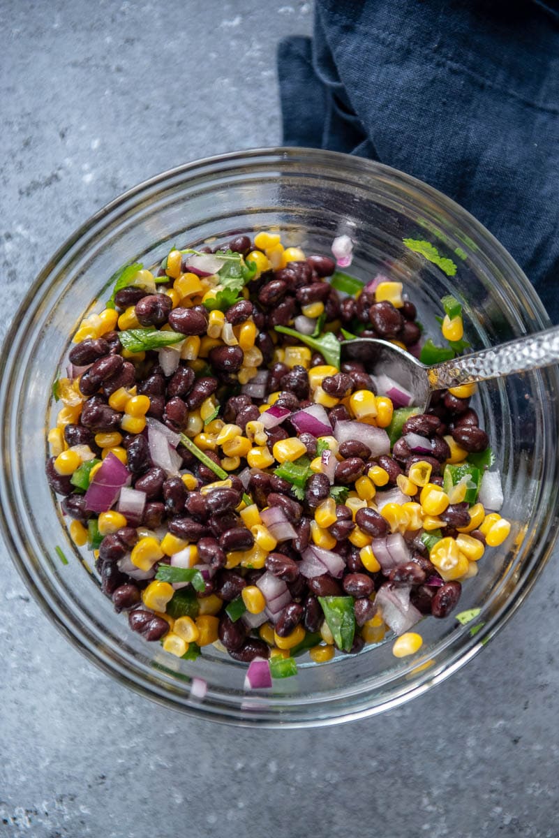 glass bowl mixing black bean and corn with onion and cilantro for salsa