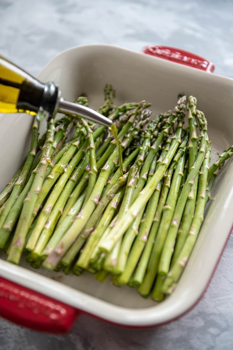 olive oil being poured on raw asparagus