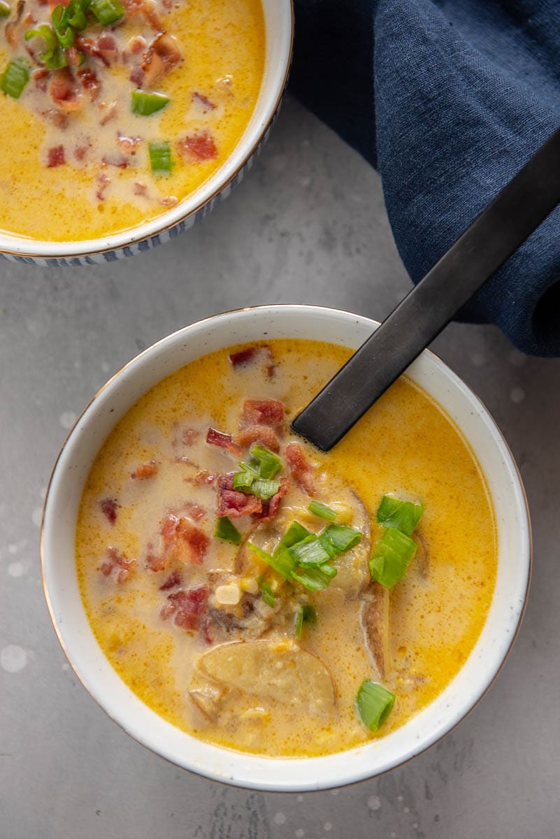 two blue and white bowls filled with corn chowder topped with crumbled bacon and green onions