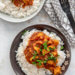overhead view of a white and brown bowl filled with white rice topped with tikka masala