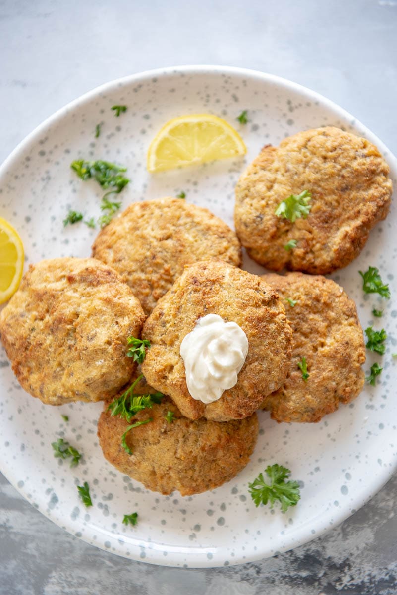 salmon patties on a white plate with lemon wedge and mayo