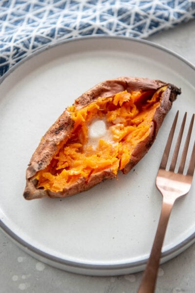 split open baked sweet potato topped with butter on a white plate