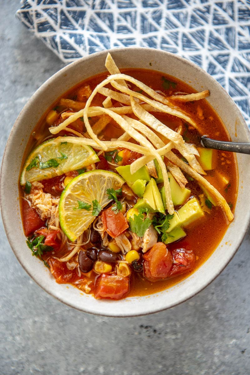 chicken tortilla soup in a bowl with lime wedges and tortilla strips