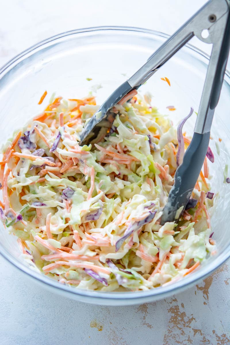 creamy coleslaw ingredients in glass bowl with tongs