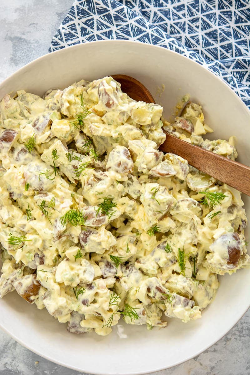 potato salad in a white bowl with a wooden spoon