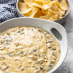 spinach dip in a white bowl with a bowl of chips