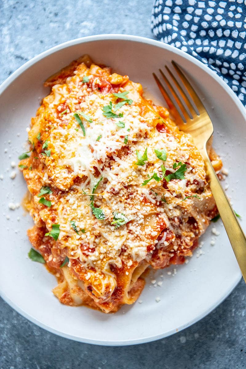 looking down at piece of lasagna in a a white bowl with gold fork