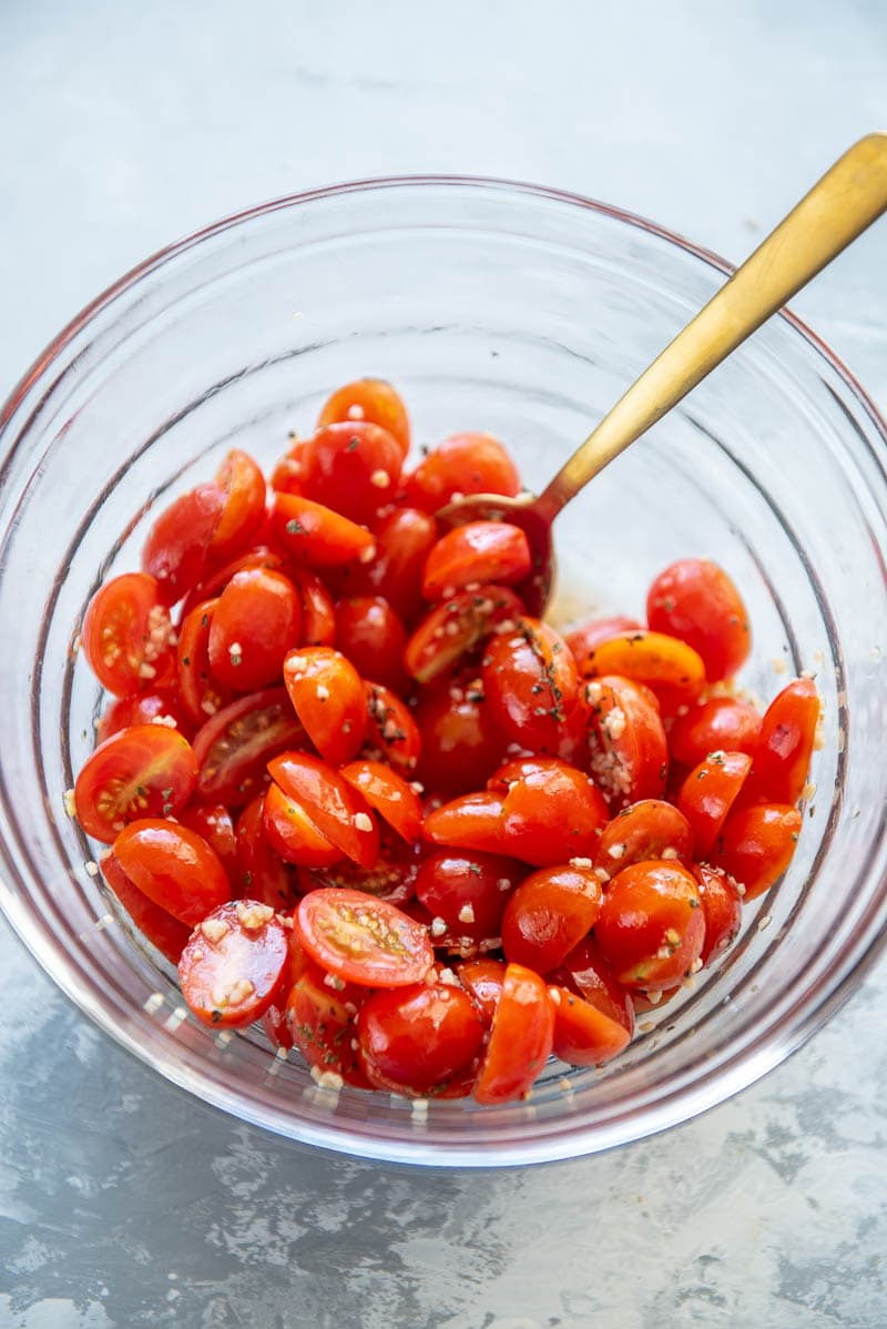 sliced grape tomatoes marinating in a bowl with a spoon