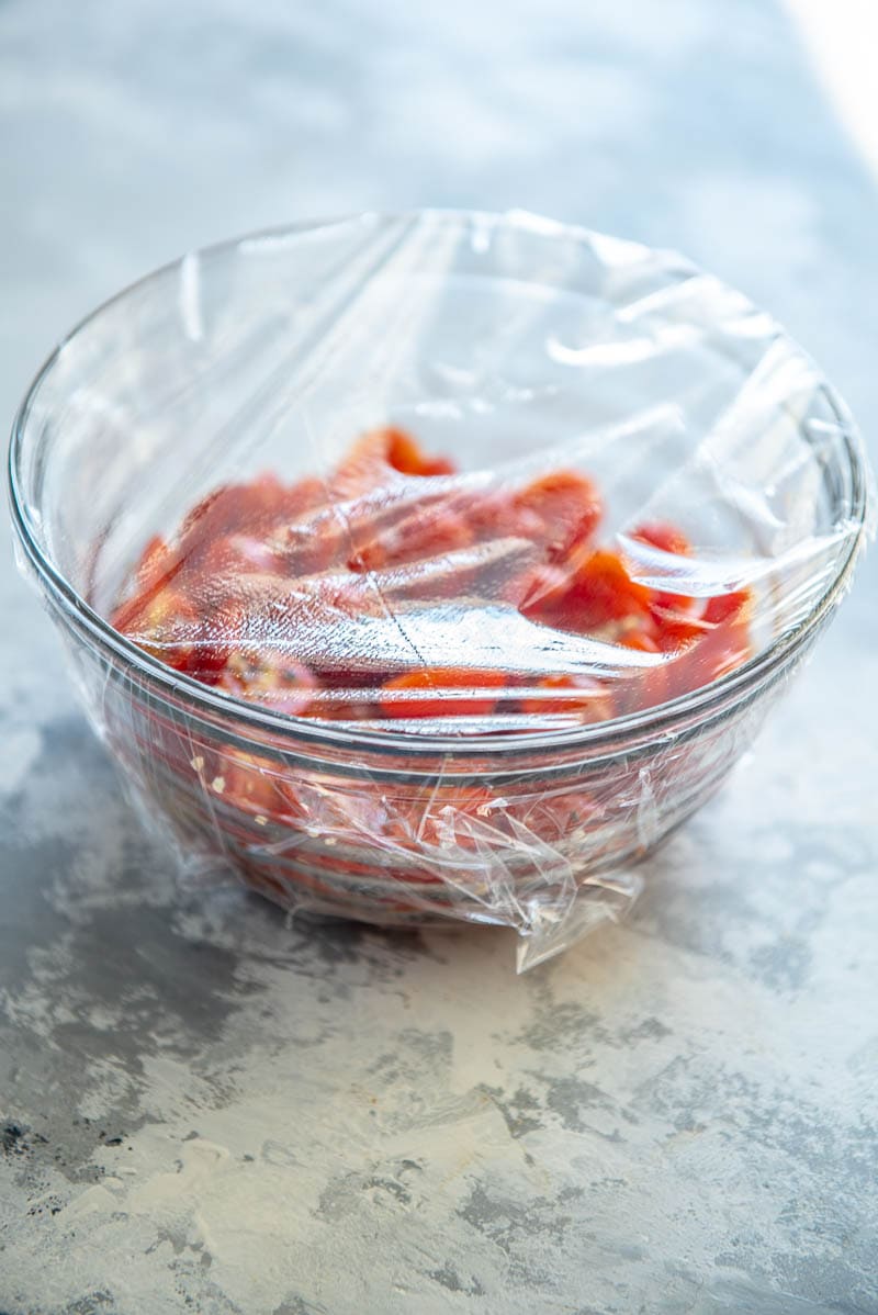 sliced grape tomatoes in a bowl covered with plastic wrap