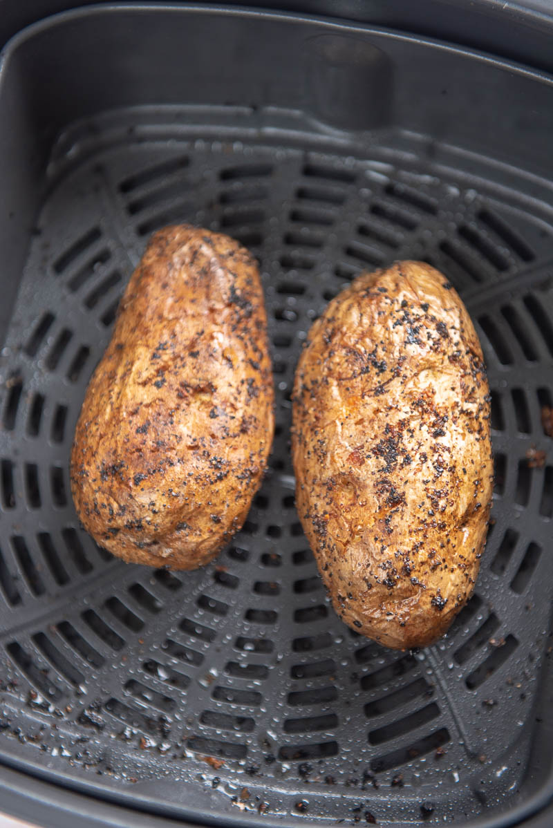 two baked potatoes in an air fryer basket