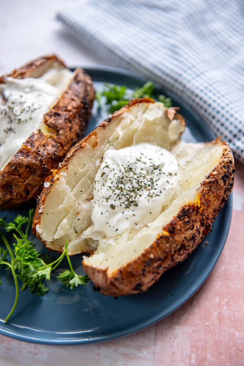 baked potato topped with sour cream on blue plate with parsley