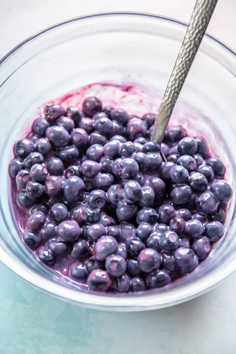 blueberries thawing in a glass bowl with a spoon