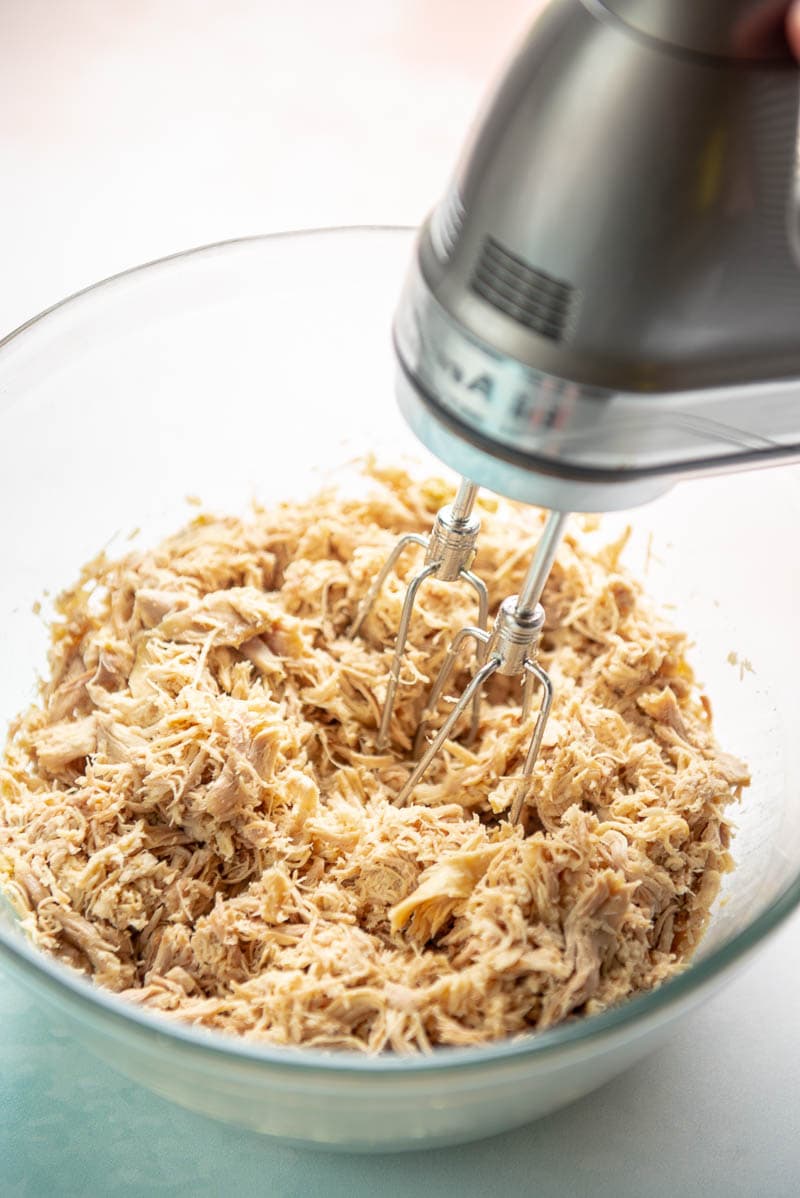 shredded chicken thighs in a bowl with electric mixer