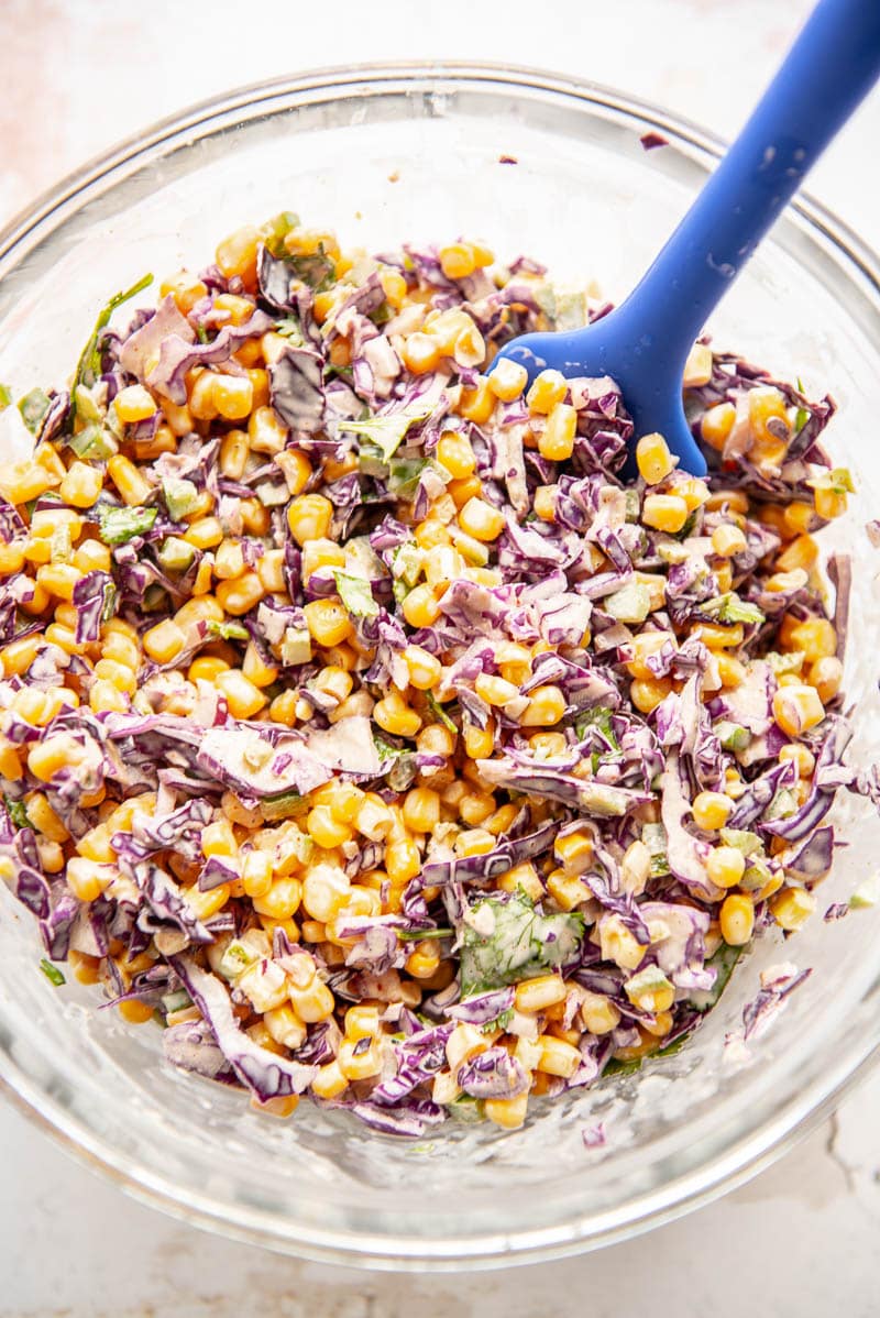 close up of corn slaw in glass bowl with spoon