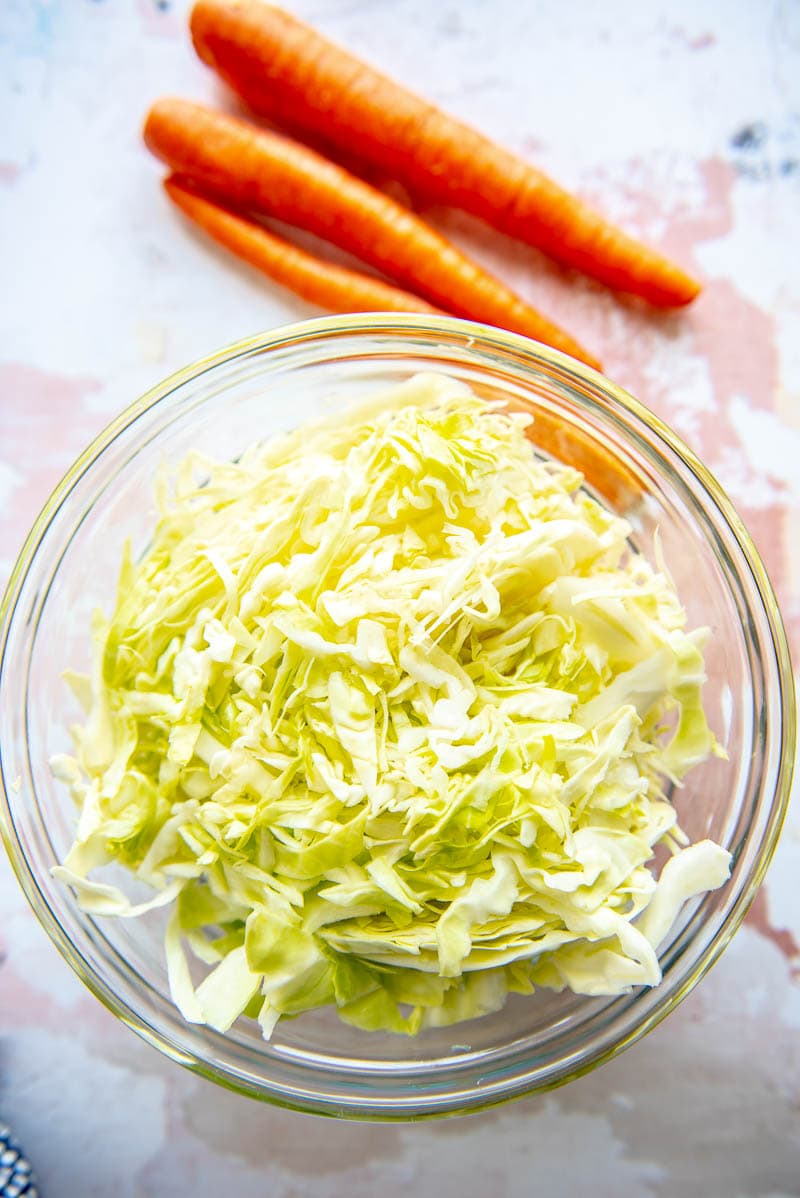 bowl of shredded cabbage next to 3 carrots