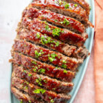 meatloaf sliced on blue platter and topped with sauce and parsley