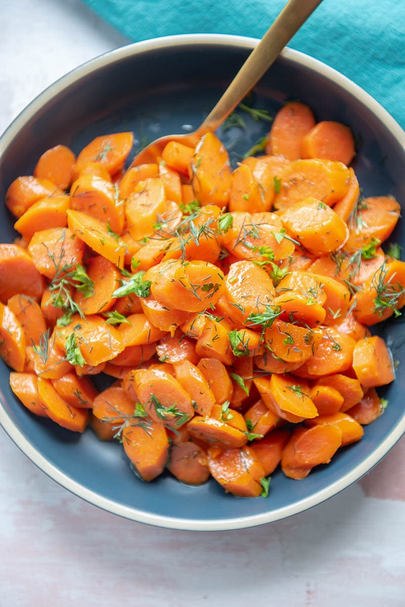 overhead view of sliced cooked carrots in a blue bowl with a gold spoon