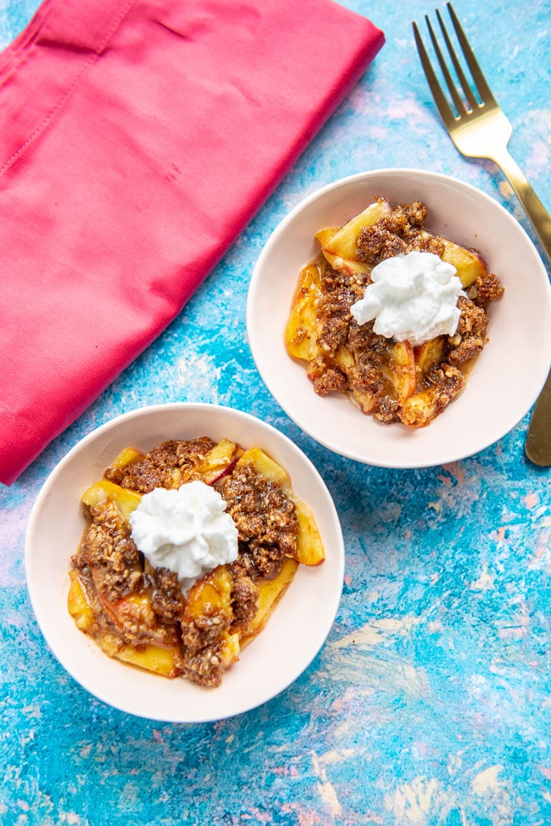 two pink bowls with individual servings of air fryer peach cobbler topped with whipped topping